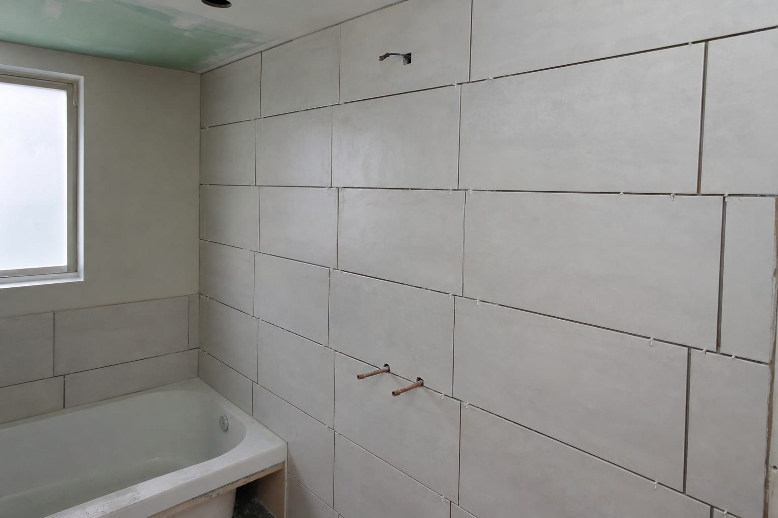 A partially finished bathroom tile installation with uneven grout lines along one wall